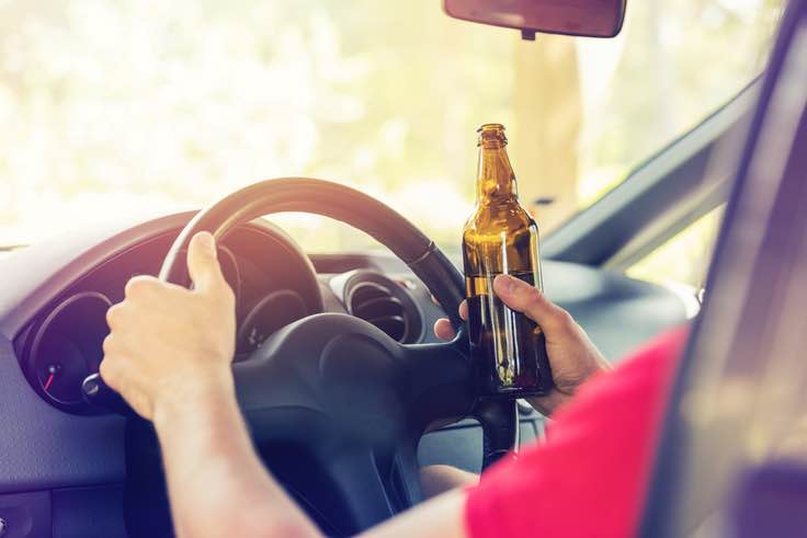 Close-up of hands on steering wheel with beer in hand